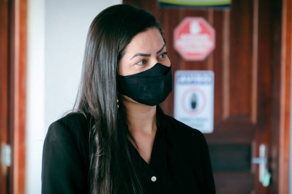 A fotografia mostra uma mulher distraída, usando máscara cirúrgica, conversando com alguém